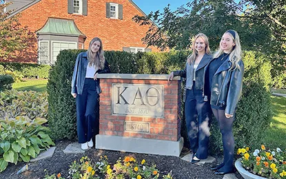 Three women in front of a Kappa Alpha Theta sign