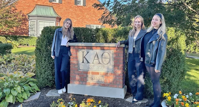 Three women in front of a Kappa Alpha Theta sign